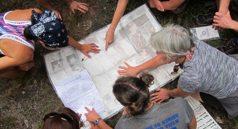 A group of people examine a map that is spread out on the ground. 